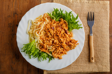 A plate of bolognese pasta decorated with herbs on a wooden table next to a linen napkin and a fork.