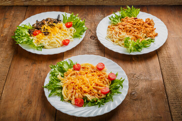 Three plates with different pasta on a wooden table.