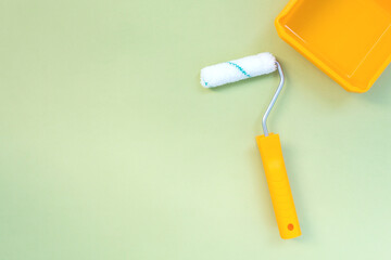 New painting roller and yellow paint tray on pastel green background