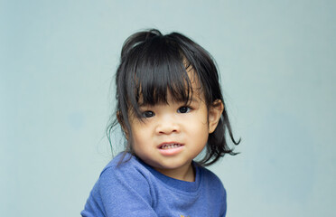 A headshot portrait of a cheerful baby Asian woman, a cute toddler little girl with adorable bangs hair, a child wearing a blue sweater smiling and looking to the camera.