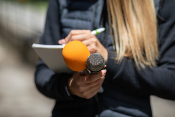 News reporter or TV journalist at press conference, holding microphone and writing notes