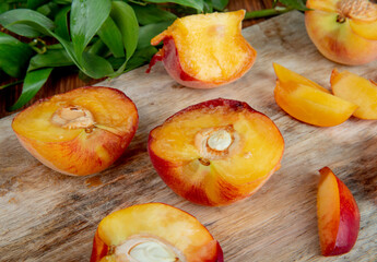 Naklejka na ściany i meble side view of halves of fresh ripe peaches on a wooden cutting board with green leaves on rustic background
