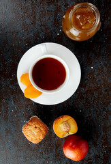 top view of a cup of tea with fresh sweet nectarine  muffin and a glass jar with peach jam on black background