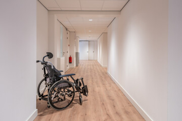An empty wheelchair stands in an empty corridor of a care home with white walls.