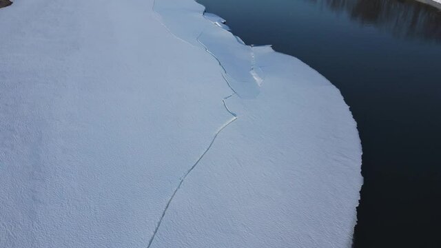 Mirror calm river flow with thick dense ice and snow sheets on its edges during the early spring melting process in northern Norway, aerial shot