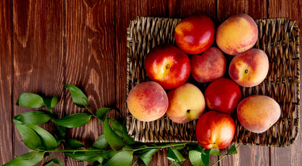 top view of fresh ripe nectarines and peaches on a wicker tray on wooden rustic background with copy space