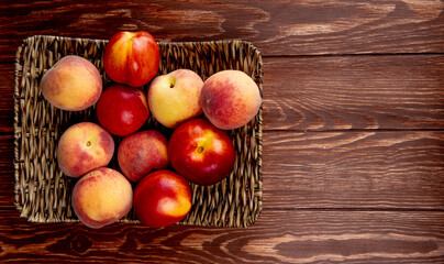 top view of fresh ripe nectarines and peaches on a wicker tray on wooden rustic background with copy space