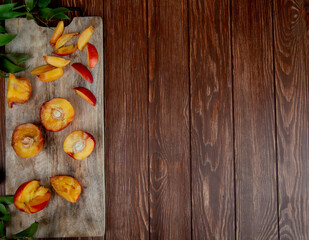 top view of halves of fresh ripe peaches on a wooden cutting board with green leaves on rustic background with copy space