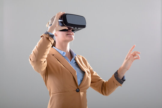 Caucasian businesswoman wearing vr headset touching virtual interface, isolated on grey background