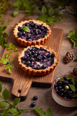Obraz na płótnie Canvas Mini tarts with blueberries and sour cream filling. Sweet homemade dessert with wild forest berries.