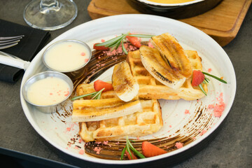 Viennese waffles with chocolate, strawberries and sauce on a white restaurant plate