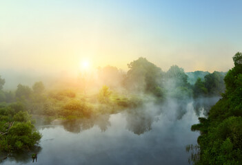 small quiet river at dawn, green overgrown coast meandering river, fog, mist over the water. Summer morning
