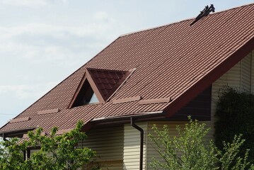 one attic window on a brown tiled roof of a house against a gray sky