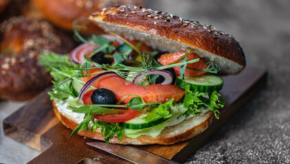Close-up New York bagel with cream cheese, salad, cucumber, herbs, olives and salted red fish. Homemade tasty sandwich salad. Appetizing and crunchy baked. Excellent breakfast or snack. Cook at home