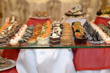 Catering a lot of sweet snacks from small cakes with cream and chocolate cream and fruit on the glass in the banquet hall
