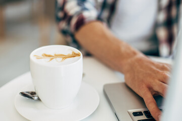 Man working, using laptop on wooden table, hands typing on keyboard, working from home or using internet to shop online