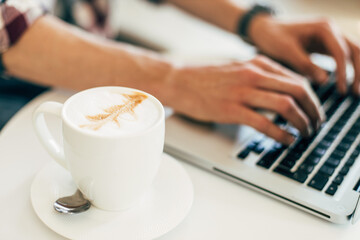 Man working, using laptop on wooden table, hands typing on keyboard, working from home or using internet to shop online