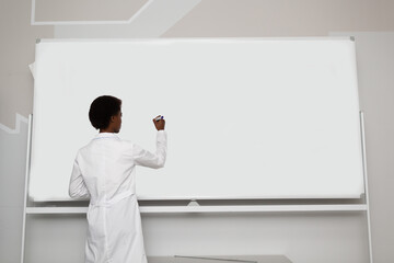 African American black woman math teacher writing on empty white board with marker rear view.