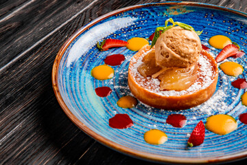 side view of apple cake with ice cream decorated with fresh strawberry and sauce on a plate on wooden background