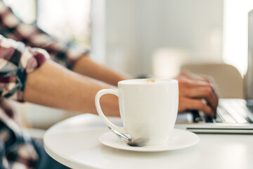 image of male hands working and typing on a laptop keyboard with a cup of coffee on a wooden table, Man working from home.