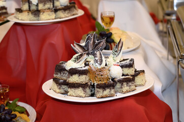 Catering plate on a red tablecloth with small brown and white cakes decorated with both white and dark chocolate