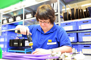 older woman assembles electronic components in a hi tech factory