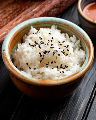 side view of boiled rice with black seeds in a clay bowl on wooden background