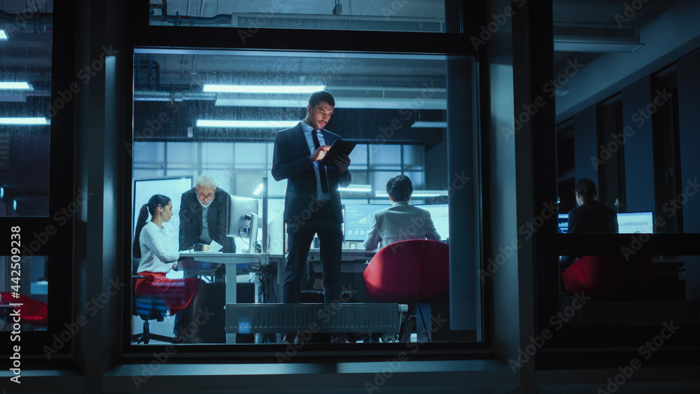 Poster Shot from Outside: Businessman Working on a Digital Tablet Computer in the Office. Manager Checking Emails while Standing by the Window. Employee Planning Financial Tasks and Business Development.