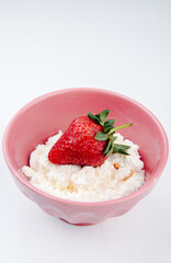side view of cottage cheese with fresh strawberry in a pink bowl on white background