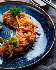 side view of crab salad with vegetables and wasabi on a plate and soy sauce on black background