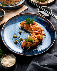 side view of crab salad with vegetables and wasabi on a plate and soy sauce on black background