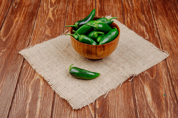 side view of fresh green chili peppers in a wooden bowl on sackcloth on rustic background