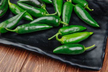 side view of fresh green chili peppers on a black tray on wooden rustic background
