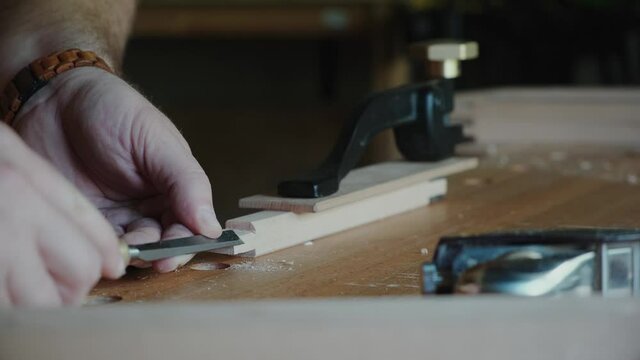 Joiner chamfer chisel on wooden parts. Carpenter working in his workshop.