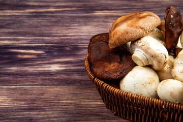 side view of fresh mushrooms in a wicker basket on rustic wooden background with copy space