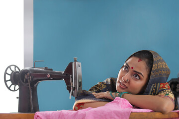 A woman thinking while sitting by the sewing machine. - obrazy, fototapety, plakaty