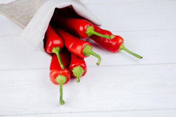 side view of fresh red chili peppers scattered from a sack on white background