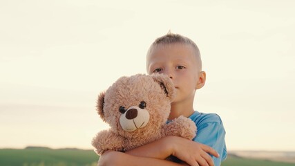 Little boy hugs his favorite soft bear toy on the playground. The child plays with the Teddy bear. Plush toy in the hands of kid in summer park. Kid plays with a toy and dreams outdoors. Best friends