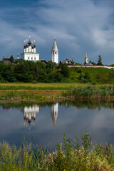 White buildings of ancient monastery in Suzdal, Russia, on bright sunny summer day, landscape, blue sky, reflection in water.