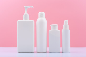 Set of white unbranded cosmetic bottles for face and body against pink background. Body cream, face oil, lotion, mask and scrub on white background. Concept of beauty treatment 
