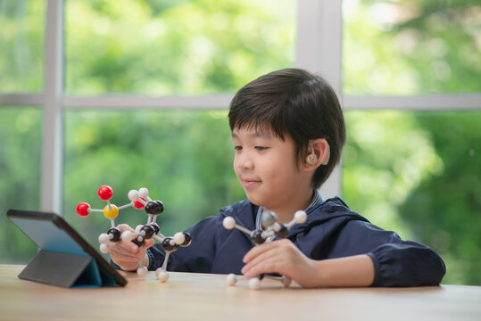 Child with hearing aid constructing molecular model  in science classroom