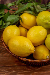 side view of fresh ripe lemons with green leaves in a wicker basket on on rustic wooden background
