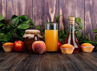side view of fresh ripe peaches with muffins peach jam in a glass jar and peach juice in a glass on rustic wooden background