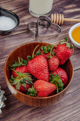 side view of fresh ripe strawberries in a wooden bowl with cookie cutters and honey on rustic background