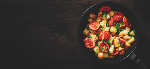 Roasted Potato and Sausage in frying pan on wooden table. Top view with copy space