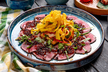 side view of fresh sliced beef pastrami served with pomegranate sauce and chopped vegetables on a plate on the table