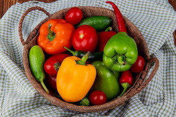 side view of fresh vegetables colorful bell peppersred chili peppers tomatoes and cucumbers in a wicker basket on plaid fabric background