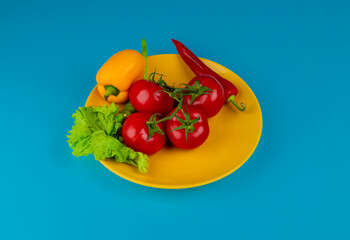 side view of fresh vegetables ripe tomatoes belle pepper and red chili pepper with lettuce on a yellow plate on blue background