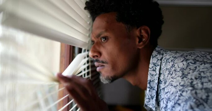 Suspicious man looking outside through window blinds