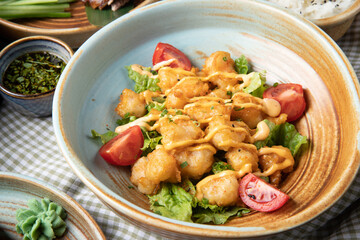 side view of fried chicken with tomatoes and sauce on lettuce on a plate on rustic background